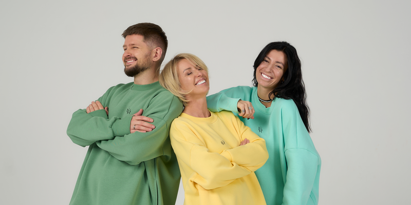 Three people wearing colorful outfits standing together against a plain background