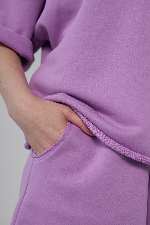 Close-up of a person wearing a purple sweatshirt with a neutral background purple