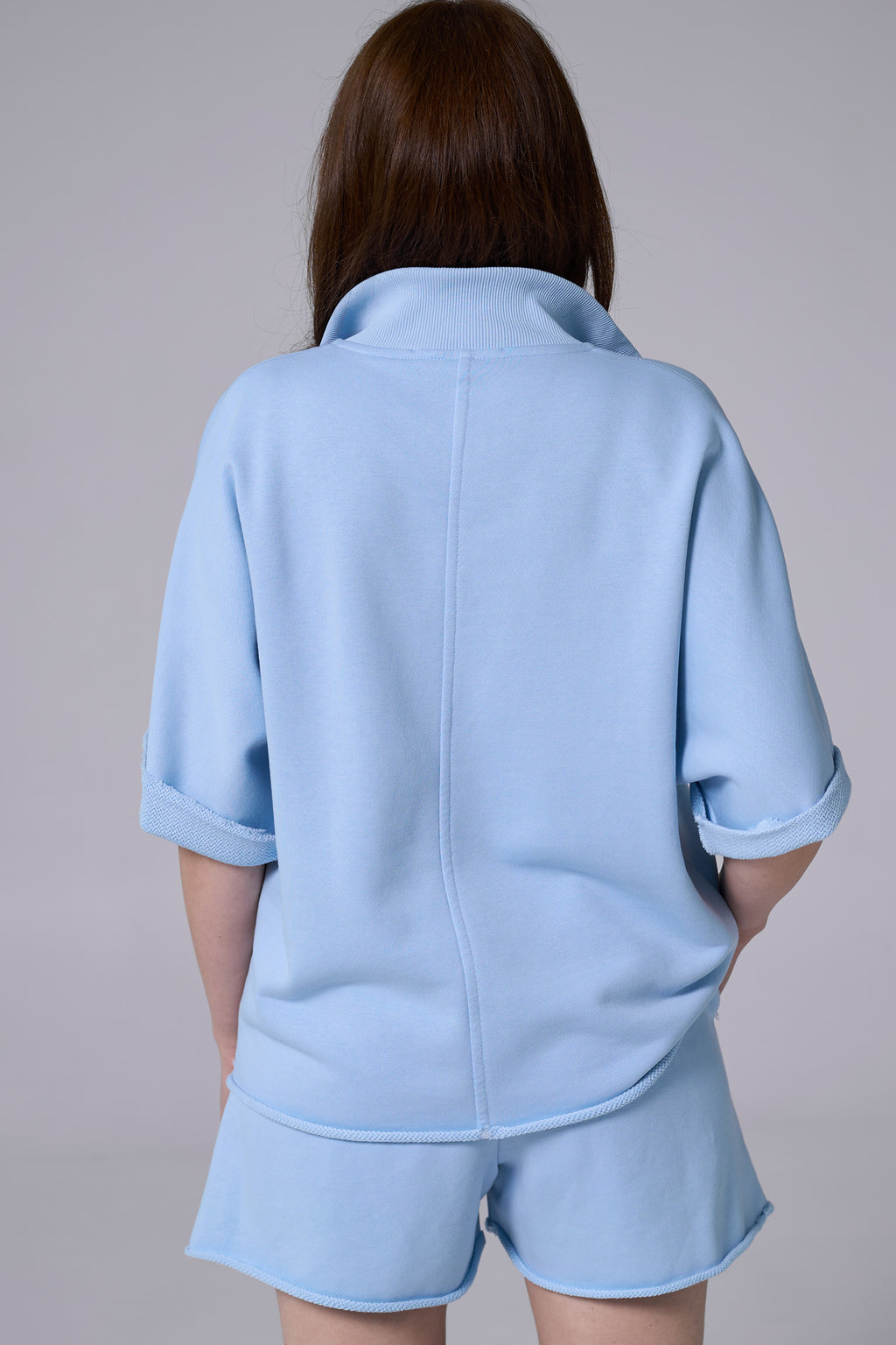 Person wearing a light blue outfit with a jacket and shorts on a plain background light blue