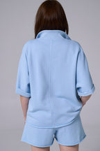 Person wearing a light blue outfit with a jacket and shorts on a plain background light blue