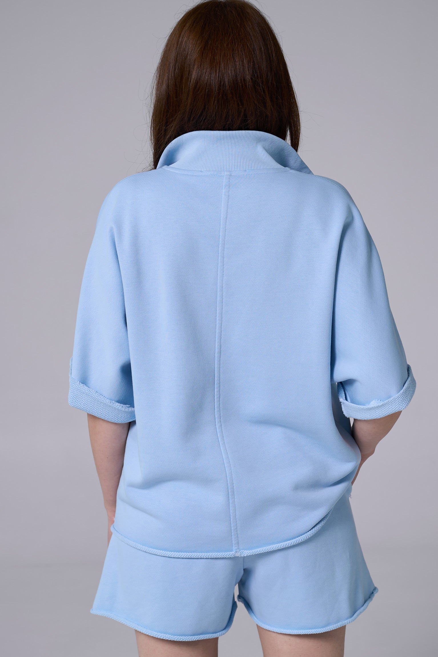 Person wearing a light blue outfit with a jacket and shorts on a plain background light blue