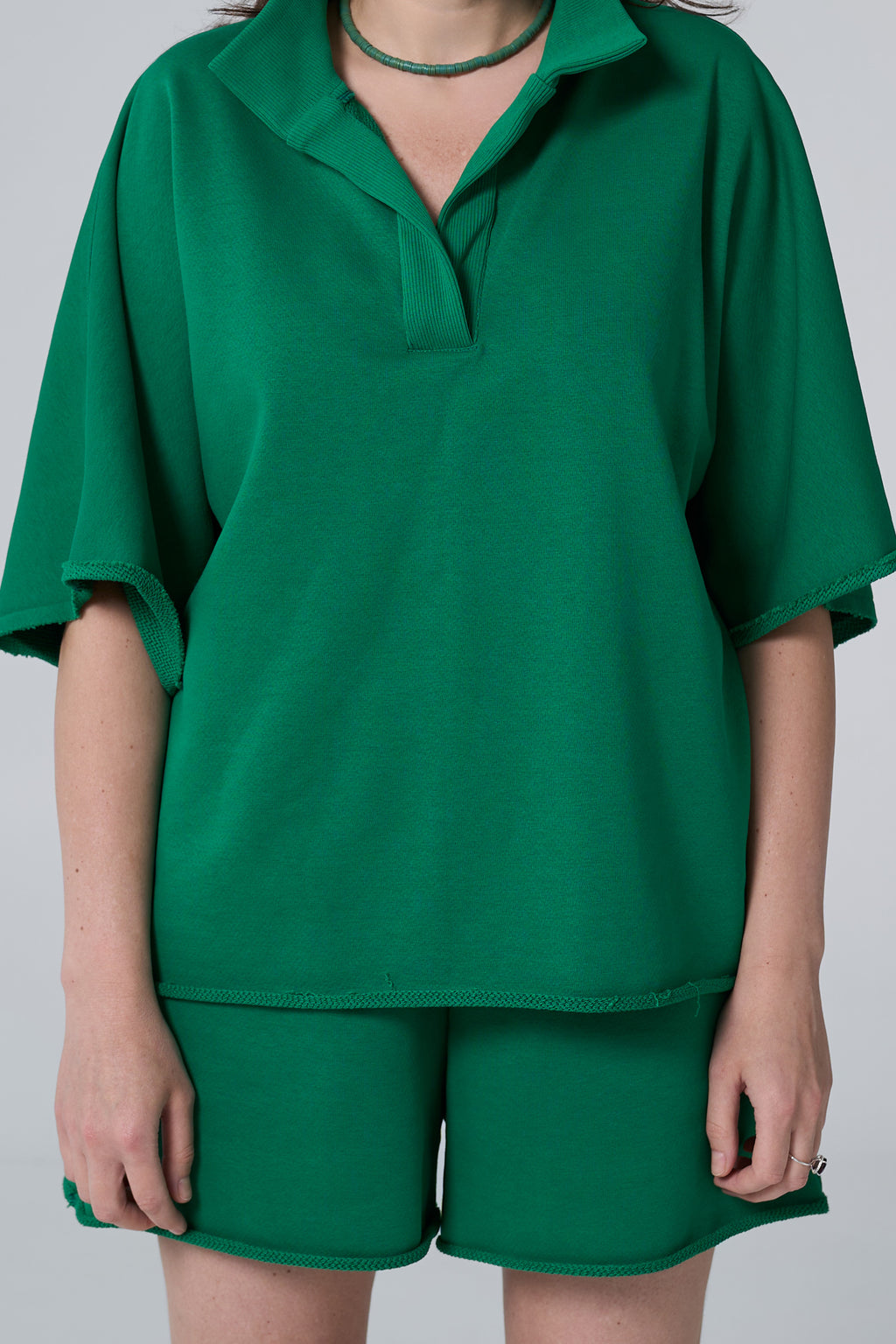 Person wearing a green outfit with a top and shorts on a plain background emerald