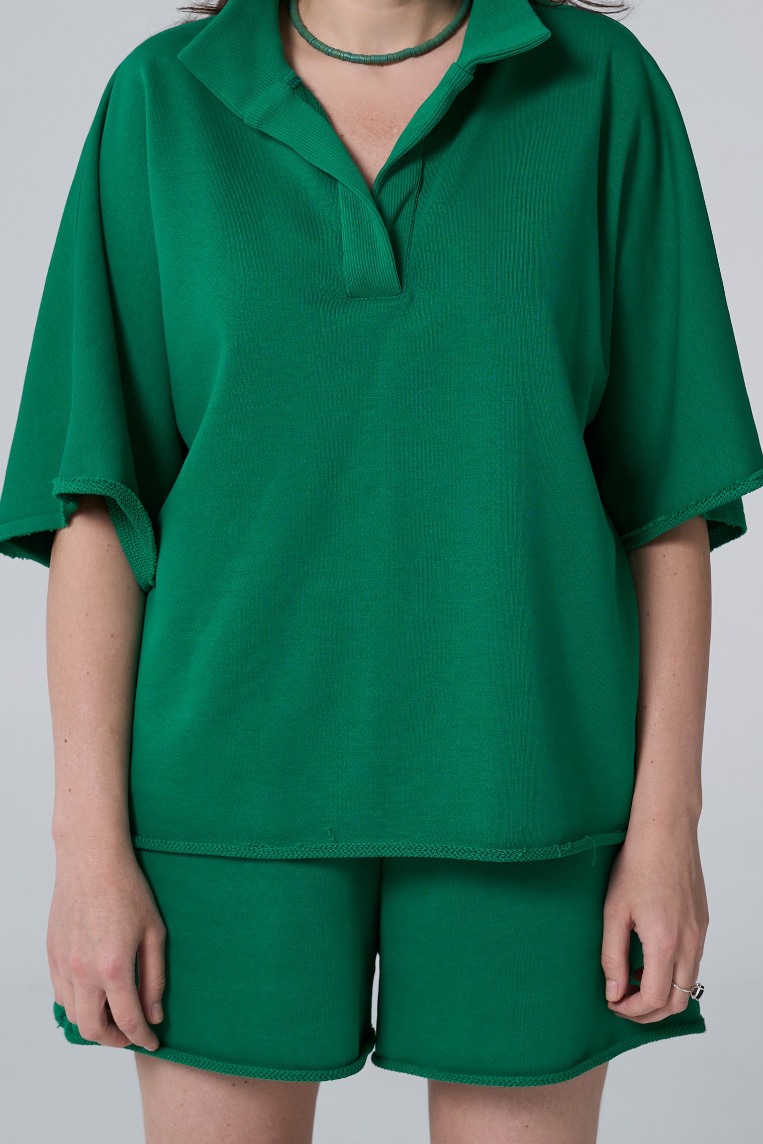 Person wearing a green outfit with a top and shorts on a plain background emerald