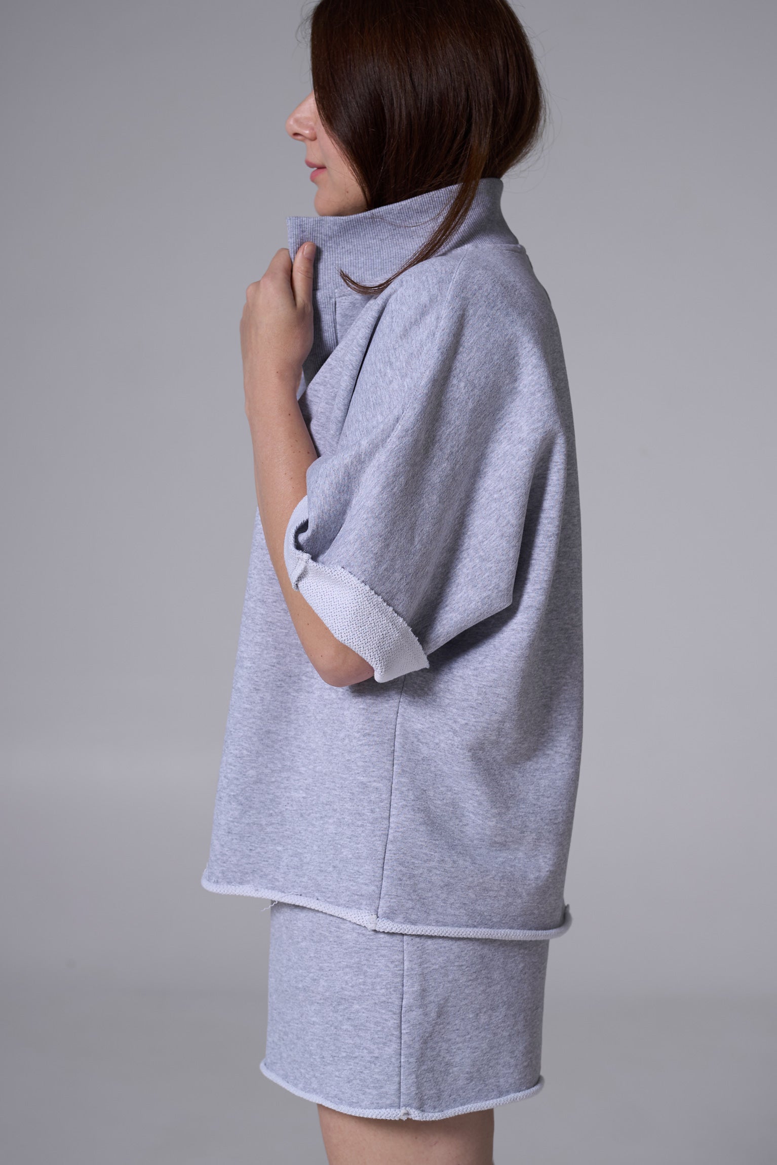 Woman wearing a gray coat over a white shirt on a plain background gray melange