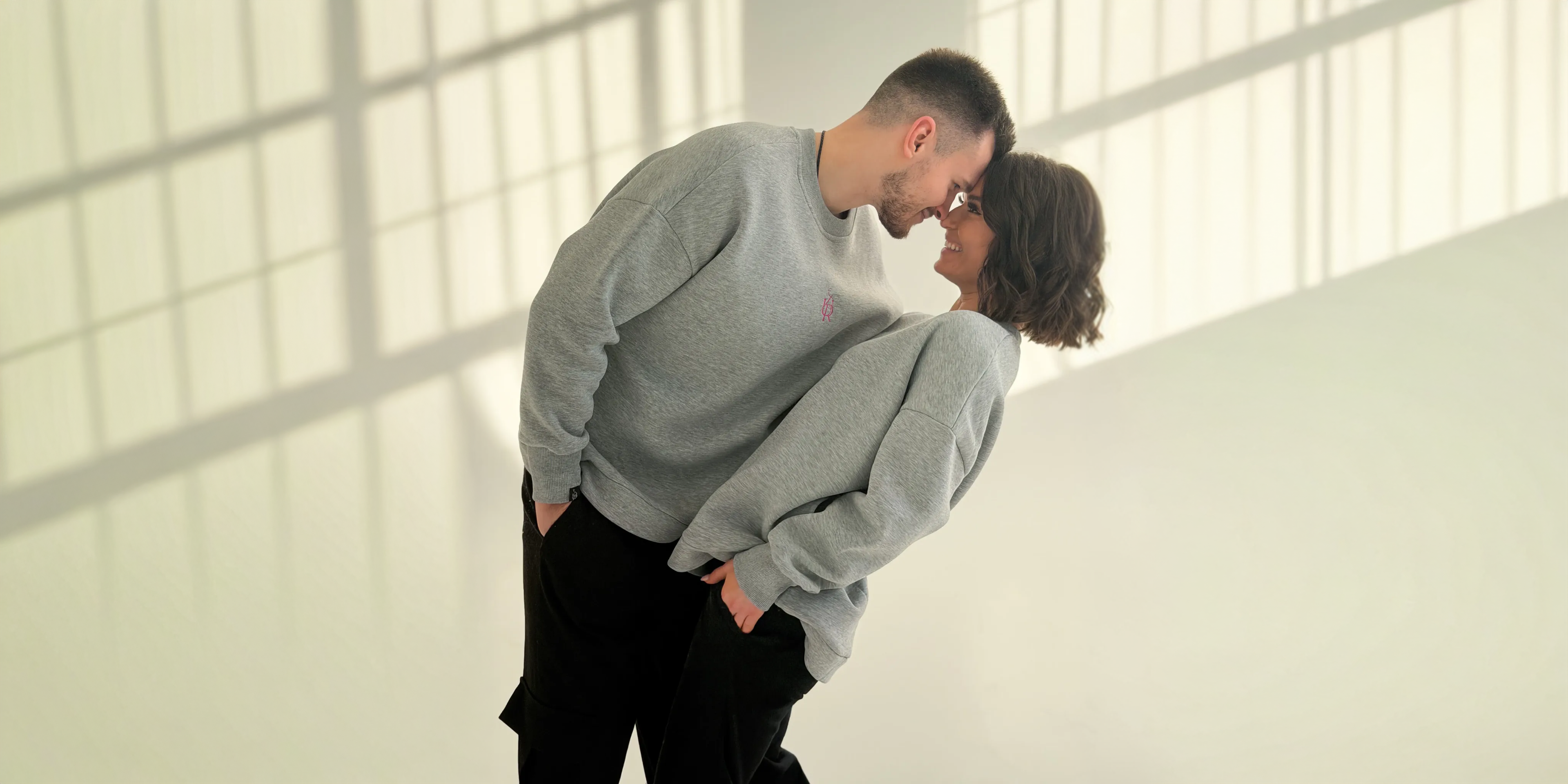 Two people embracing in a modern indoor setting with large windows.